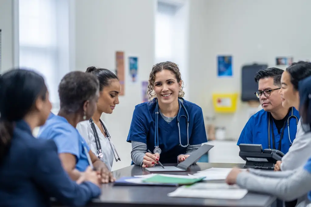 A smiling nurse in navy scrubs at a table with the rest of the clinical team